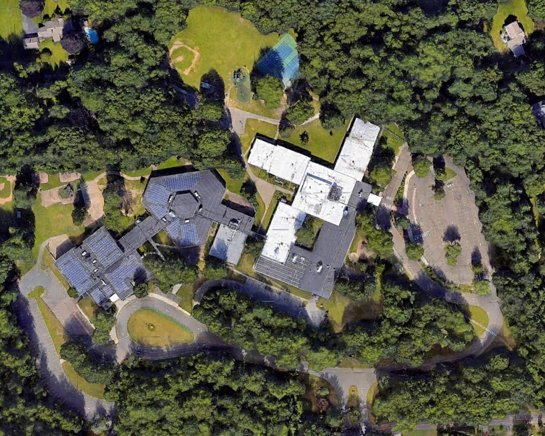 Aerial view of the Beecher Road School campus in Woodbridge, Connecticut: the school buildings and parking lots set among playing fields and wooded residential neighborhoods.