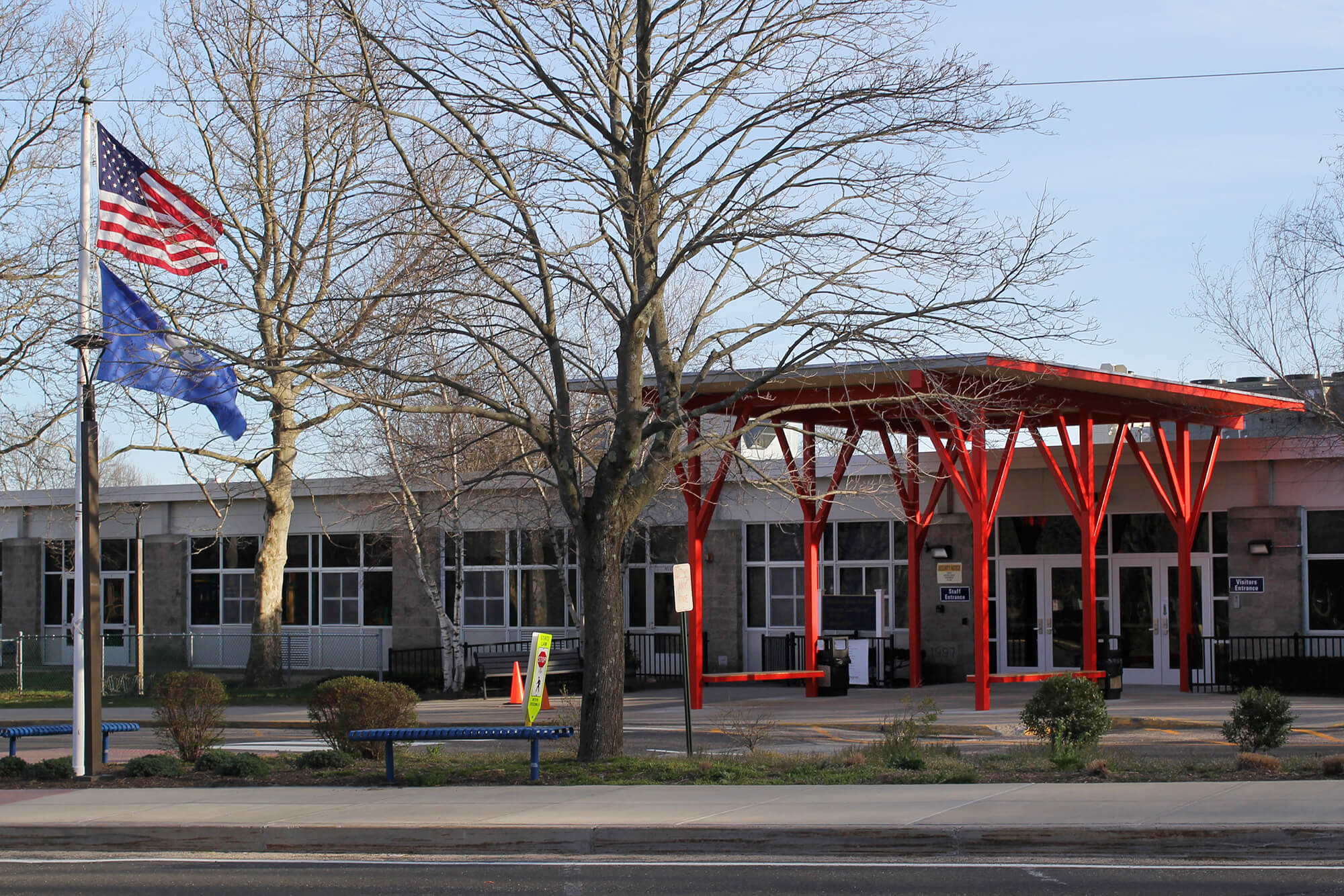 Beecher Road School seen from the street — a long brick building with a red steel entry canopy, U.S. and Connecticut flags, and bare winter trees in front.